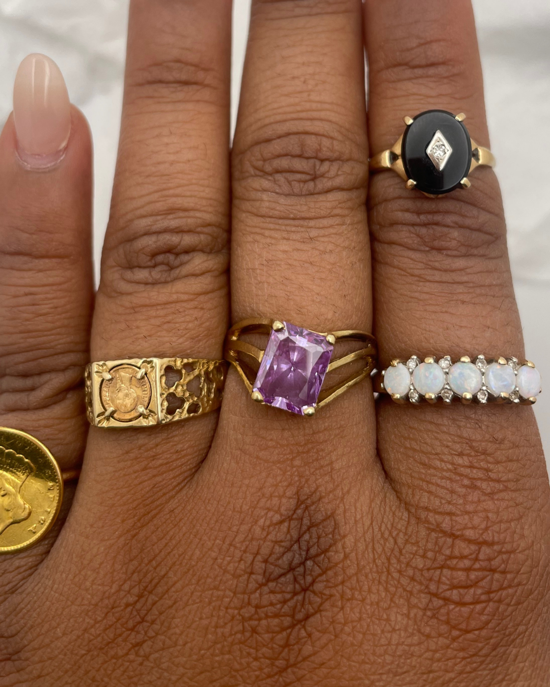 Close-up of a hand wearing multiple gold rings with different designs on a neutral background